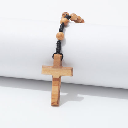 Plain olive wood cross hanging over a white block with two prayer beads above