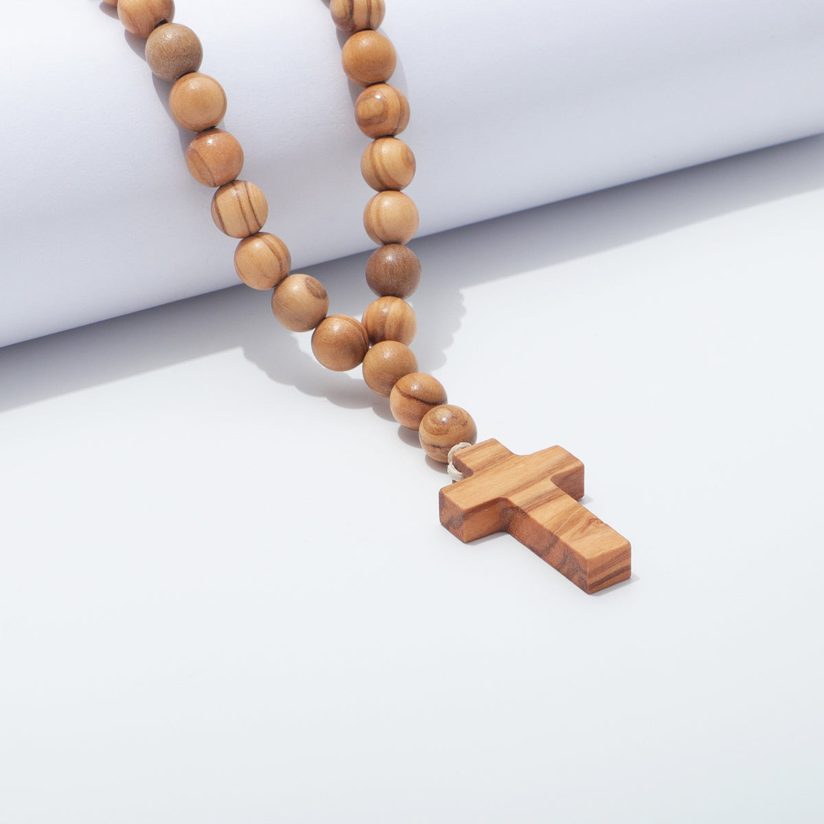 Close view of 10 mm olive wood beads on light cord beside the wooden cross