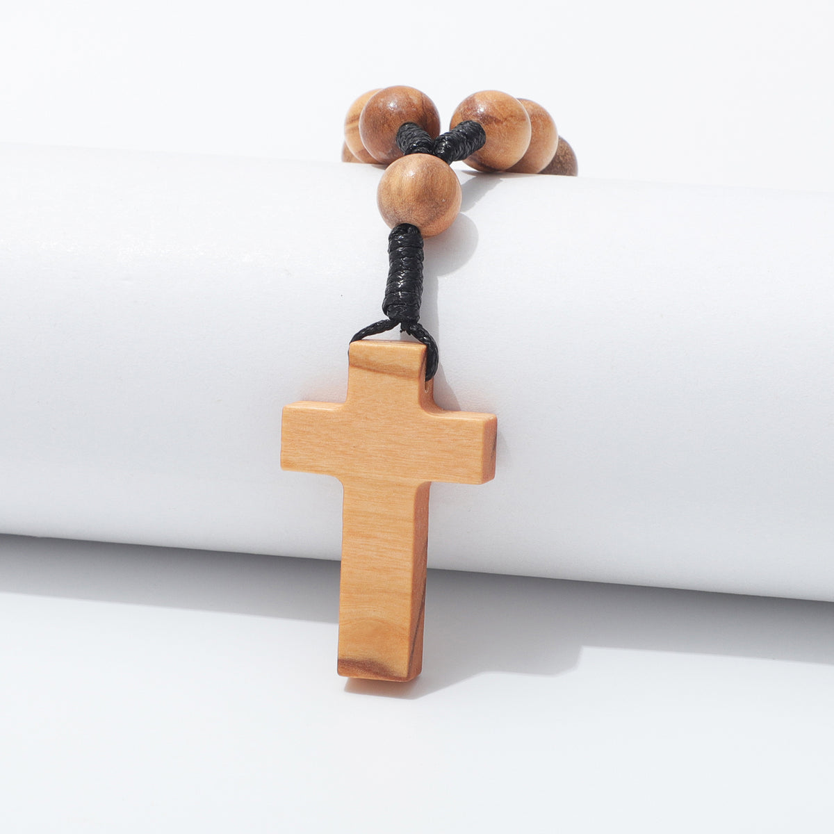 Plain olive wood cross hanging over a white block with a prayer bead and black cord above