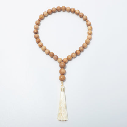 Full front view of olive wood prayer beads with two small dividers and three beads above a cream tassel